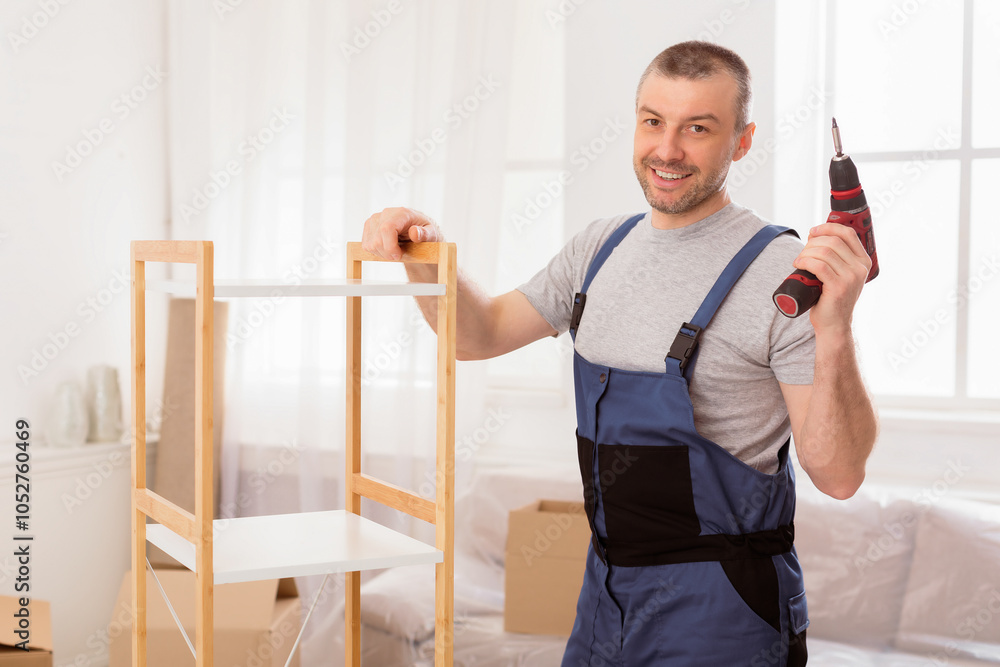Poster furniture assembler man posing with electric drill assembling cabinet working indoor, smiling to cam