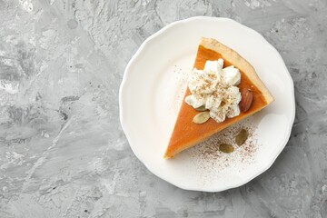 Piece of tasty homemade pumpkin pie with whipped cream, seeds and almond on grey table, top view. Space for text