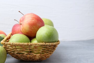 Fresh ripe apples in wicker basket on grey table, closeup. Space for text