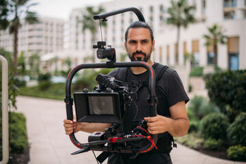 Director of photography with a camera in his hands on the set. Professional videographer at work on filming a movie, commercial or TV series. The filming process on the street, on location