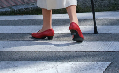 Elderly woman’s feet in bright red shoes walk with a cane on a pedestrian
