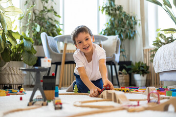 A European child plays with a wooden railway and colored blocks at home. 