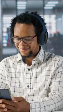 Vertical video African american general manager reviews forecasts while he listens to music on headset, feeling relaxed and multitasking at his desk. Data analyst focuses on objectives, strategy