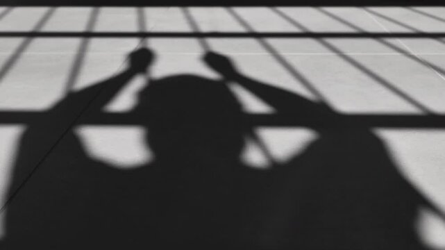 shadow of angry prisoner shaking beating cell bars in prison