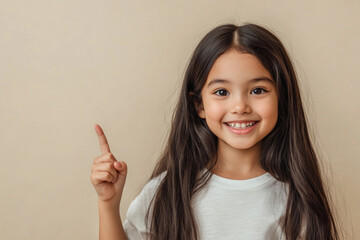 Little girl with long brown hair and white shirt smiles and points at the camera.
