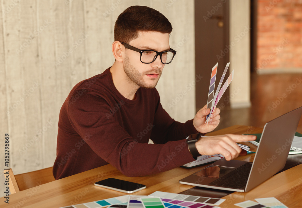 Poster designer at work. freelancer guy working on laptop choosing color samples sitting in modern office. 