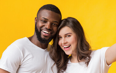 Happy Interracial Couple Taking Selfie, Sincerely Smiling And Posing Together Over Yellow Background