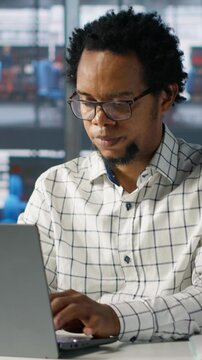 Vertical video African american general manager reviews business forecasts and plans on his laptop at office desk, strategy planning. Data analyst focuses on company objectives and resource allocation