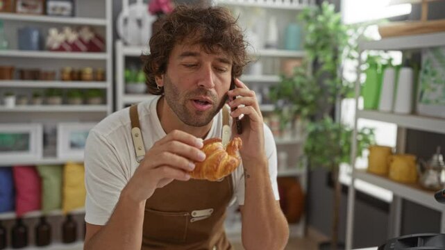 Young man eating croissant while talking on mobile phone in a home decor store with stylish interior design