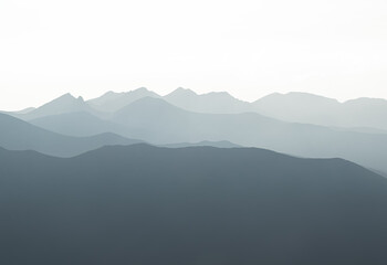 Sunset over the Tatra Mountains, showcasing serene layers of mountain peaks fading into the misty...