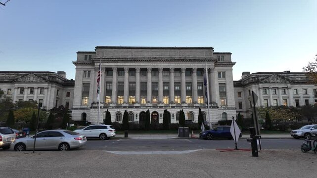 A white marble building with columns, windows, and a sign reading United States Department of Agriculture. There are bushes and trees in front of the building. The sky is blue and there is a flagpole 