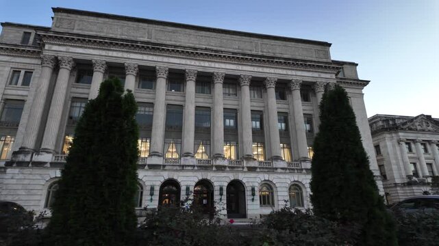 A white marble building with columns, windows, and a sign reading United States Department of Agriculture. There are bushes and trees in front of the building. The sky is blue and there is a flagpole 