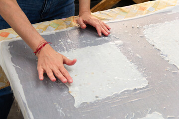 Close-up of unrecognizable woman hands in the process of making recycled paper sheets from paper pulp put on a fabric sheet to dry. Zero waste, recycling, ecology concept.