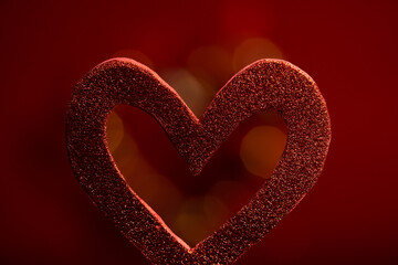 forma de corazón recortado de material texturizado con fondo rojo desenfocado 