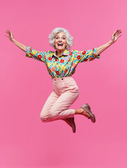senior woman jumping in the air with arms raised on pink background, generative ai