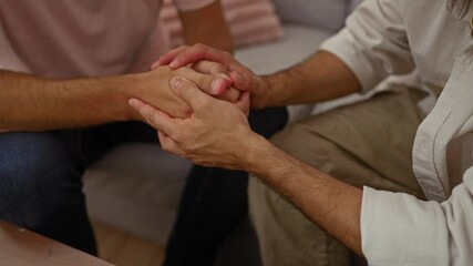 Men holding hands in a living room showing support and empathy, demonstrating a personal relationship within a home setting