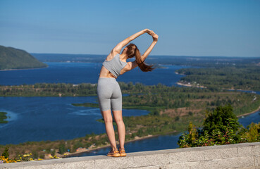 A young woman in a tracksuit performs physical exercises in a summer park