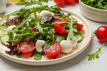Tasty salad with arugula, lettuce, mozzarella cheese and vegetables on white table, closeup