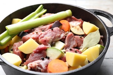 Cooking stew. Uncooked meat and vegetables in pot on white tiled table, closeup