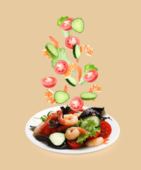Shrimps and other ingredients falling onto plate on dark beige background