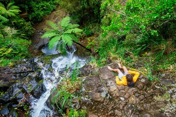Boy sitting on the edge of a waterfall at the Fairy Falls Walk, Henderson, Auckland, New Zealand.