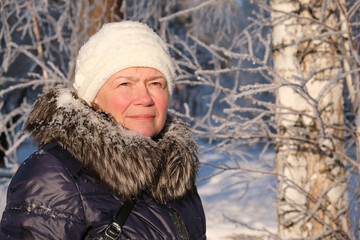 Senior woman enjoying a winter day in the nordic forest. Warm clothes, padded jacket with fur