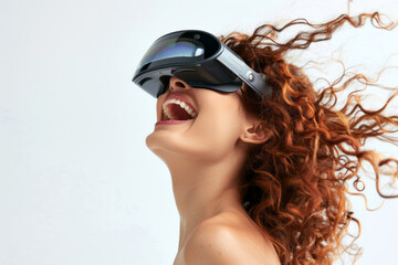 Fototapeta premium A beautiful woman wearing VR glasses, laughing with curly hair flying in the wind against a white background, showing her teeth from a side view, depicting the concept of virtual reality technology.