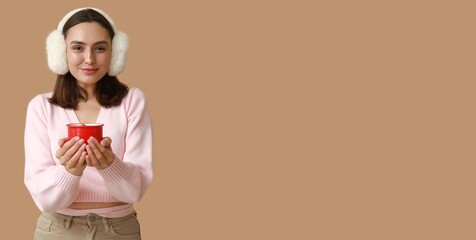 Beautiful young woman holding mug of hot mulled wine on beige background with space for text