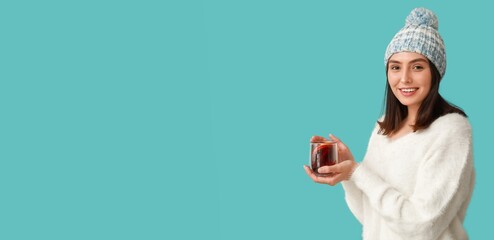 Happy young woman holding glass cup of hot mulled wine on blue background with space for text