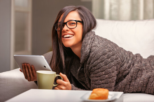 Happy woman using tablet and drinking coffee on sofa at home
