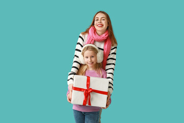 Fototapeta premium Cute little girl and her mother with Christmas gift box on blue background