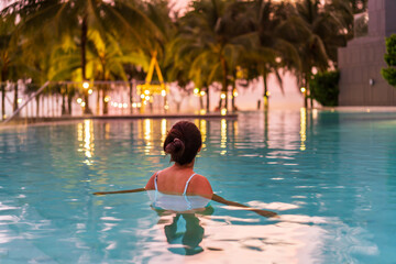 Young woman traveler relaxing and enjoying the sunset by a tropical resort beachfront pool while...