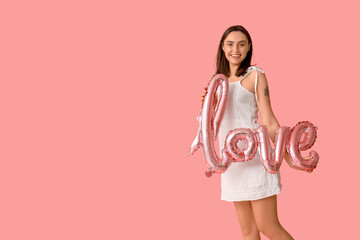 Beautiful young woman with air balloon in shape of word LOVE on pink background. Valentine's Day celebration