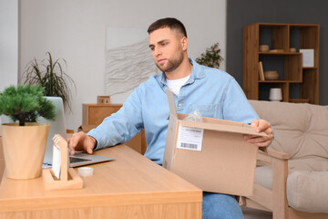 Young man with open parcel using laptop at home