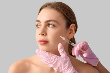 Pretty young woman receiving filler injection in face on grey background
