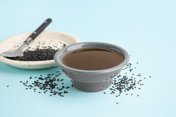 Bowl of oil and plate with sesame seeds on blue background