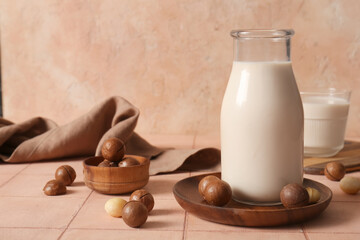 Bottle and glass of fresh macadamia milk on beige tile table