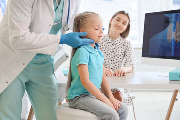 Male endocrinologist examining thyroid gland of little girl and her mother in clinic