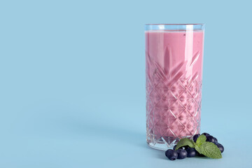 Glass of fresh blueberry smoothie with mint and berries on blue background