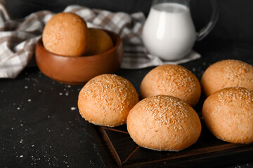 Wooden board and bowl of fresh buns with sesame seeds on black background