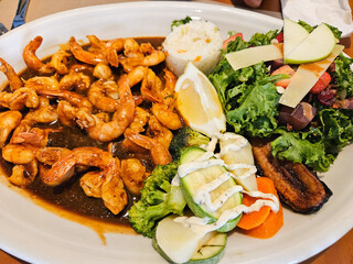 A plate of food with shrimp, broccoli, and carrots. The plate is white and the food is colorful