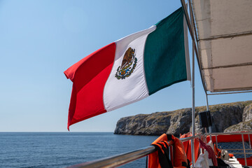 Mexican flag flying in the foreground. Out of focus in the background Marietas Island -...