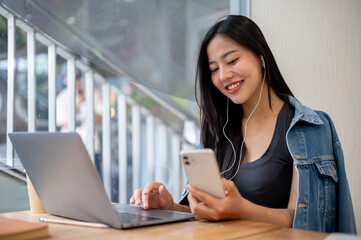 A woman is using her laptop and smartphone while sitting in a coffee shop, working remotely.