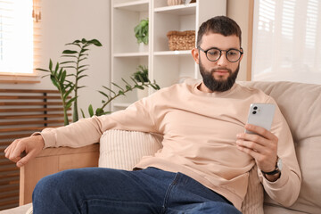 Young bearded man working with mobile phone on sofa at home