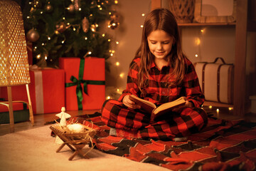 Little girl reading Christmas story on plaid at home in evening