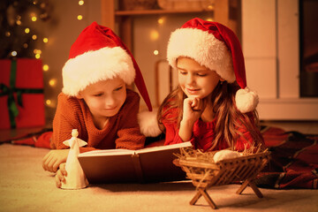 Little children reading Christmas story at home in evening