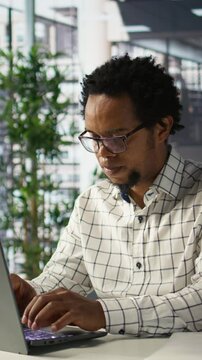 Vertical video African american general manager reviews business forecasts and plans on his laptop at office desk, strategy planning. Data analyst focuses on company objectives and resource allocation