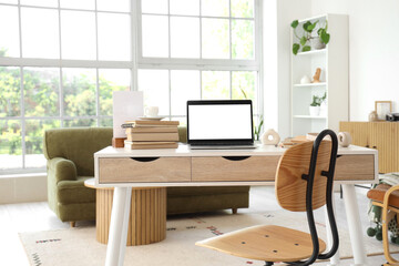 Blank laptop with books on programmer's desk in light living room