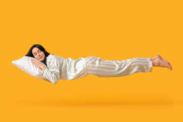 Pretty young woman flying while sleeping on yellow background