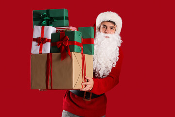 Young Santa Claus with Christmas presents on red background